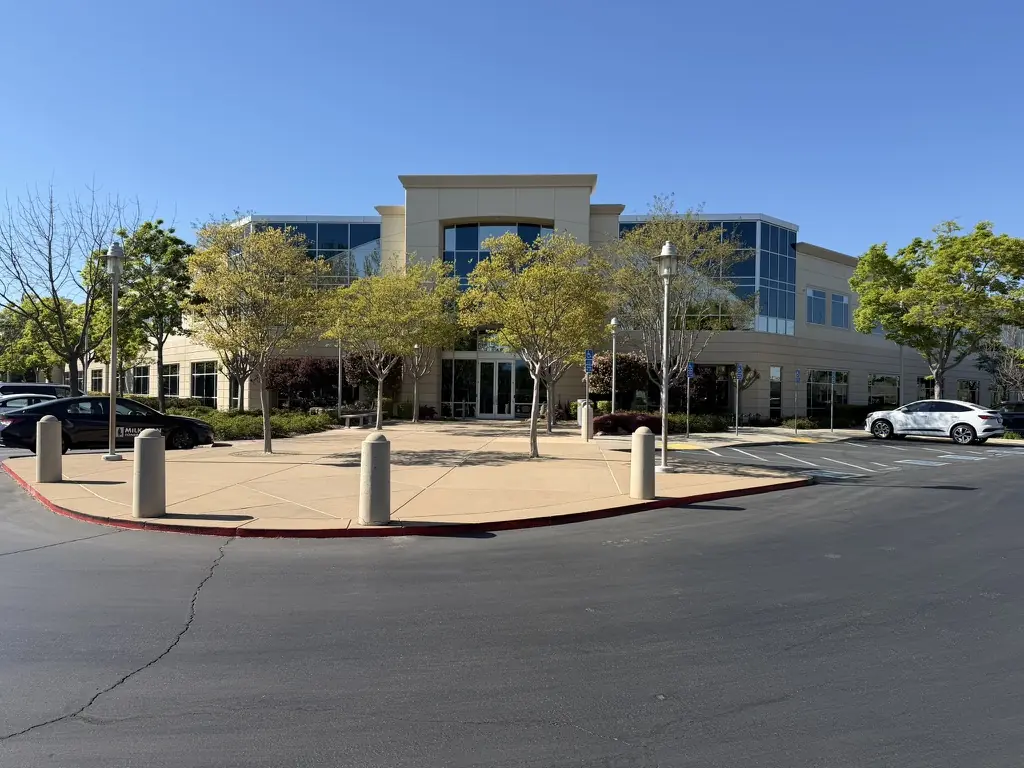 Front of the 1430 Blue Oaks Blvd building: a two-story office building with tall glass windows, trees, and a plaza.