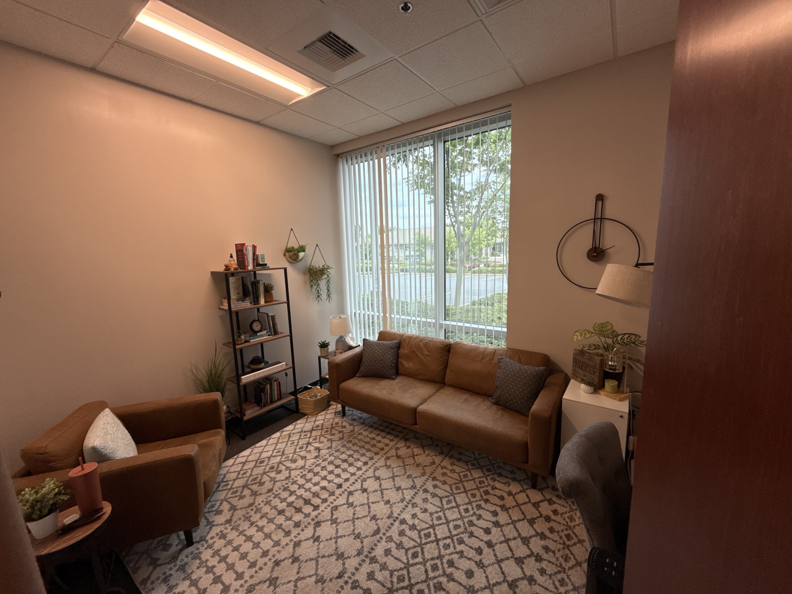 Office #5: tan leather sofa and chair, a geometric rug, and a window looking onto Blue Oaks.
