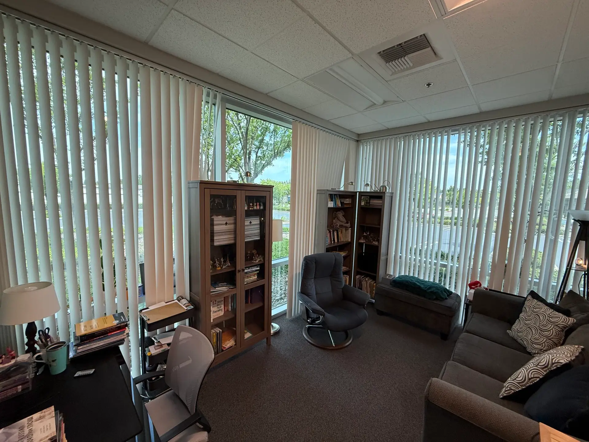 Office #4: corner room with two windows, a grey sofa, and a bookcase.